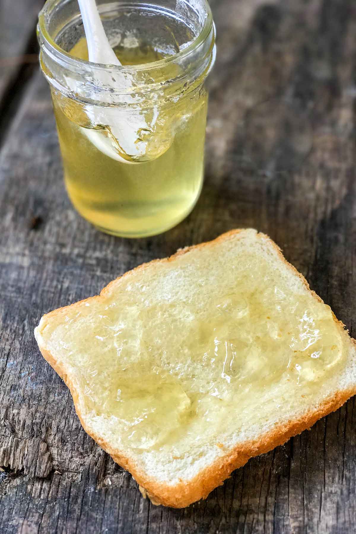 Honeysuckle Jelly spread on bread with jar in the back.